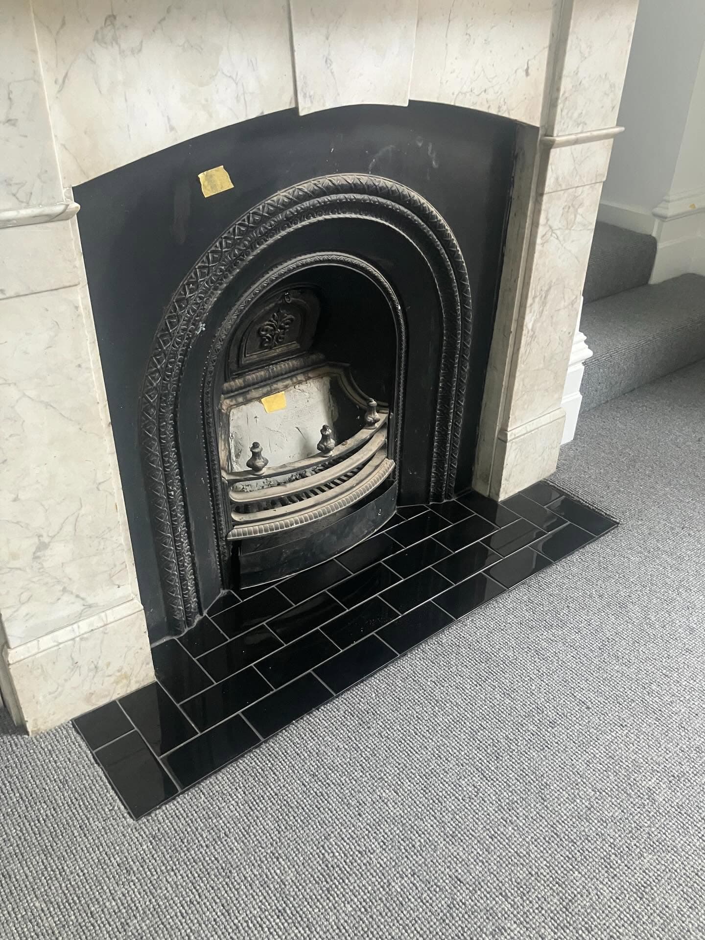 Cast-iron fireplace insert set into a pale stone surround, with a black tiled hearth on a speckled floor