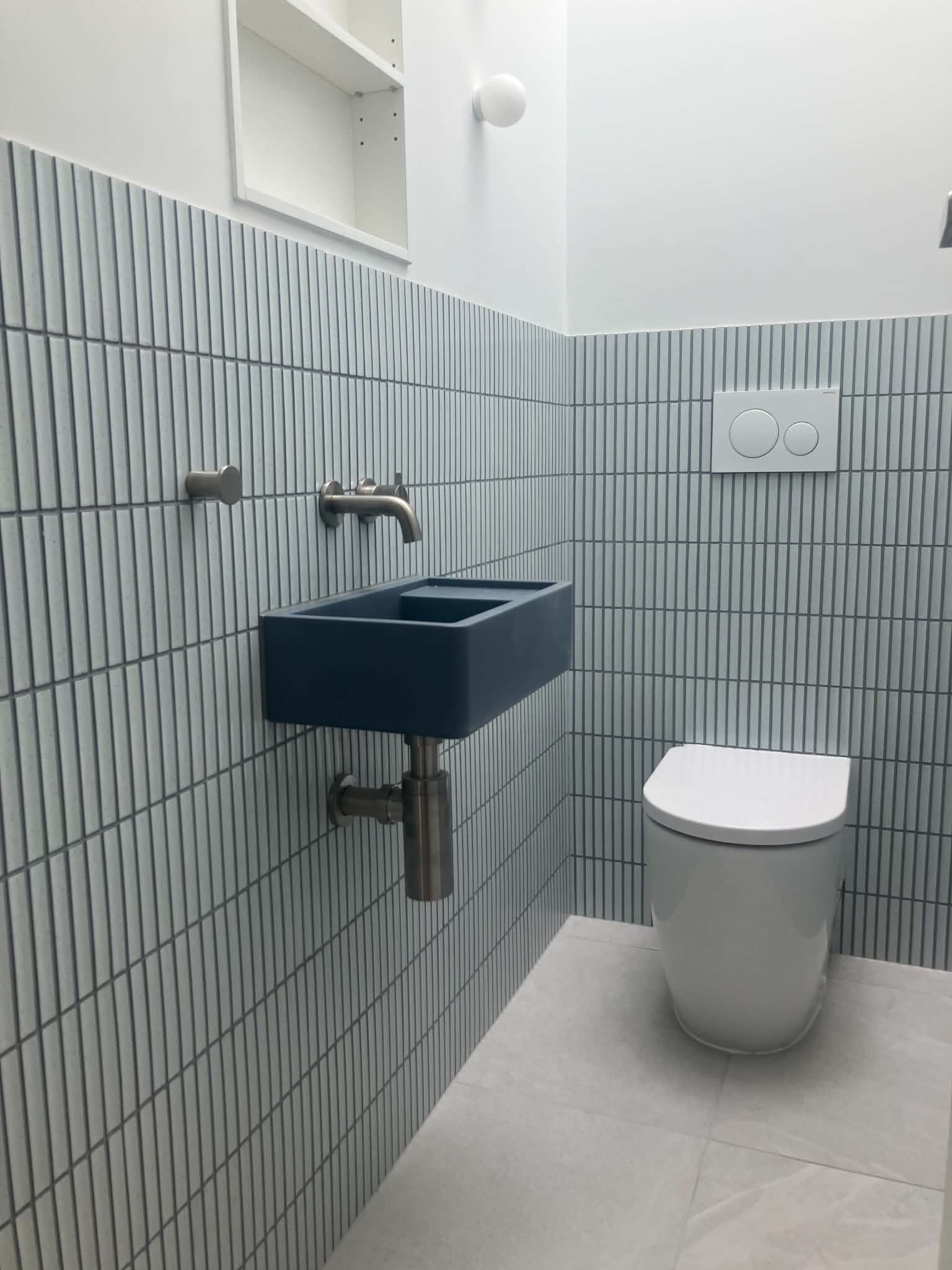 Pale blue tiles stacked vertically behind a wall-hung basin and toilet