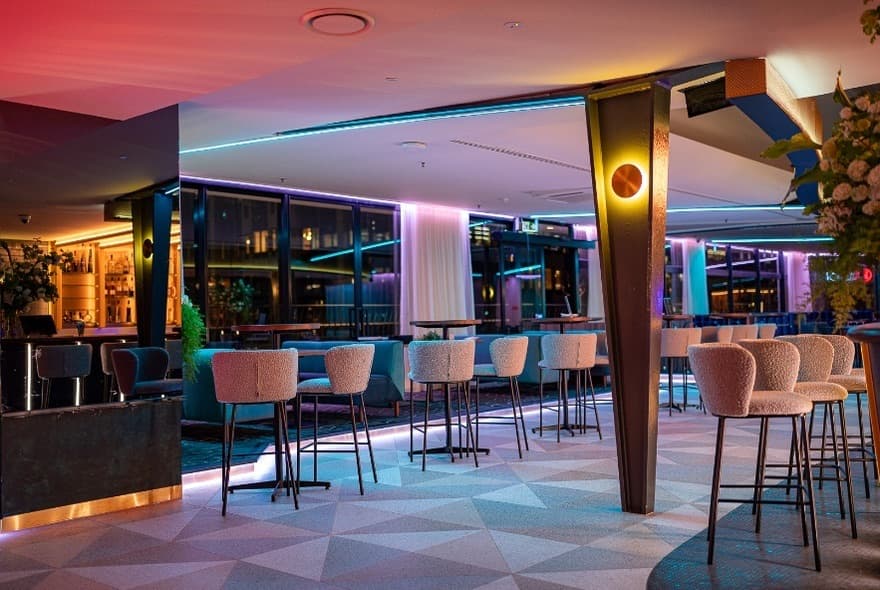 Fitted-out bar interior with a patterned tiled floor, banquette seating and stools under coloured lighting