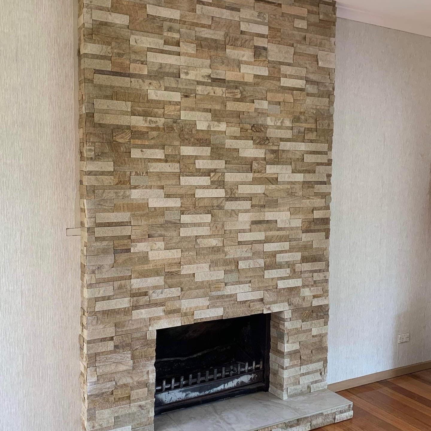 Fireplace clad in stacked stone with mitred external corners, above a black stone hearth