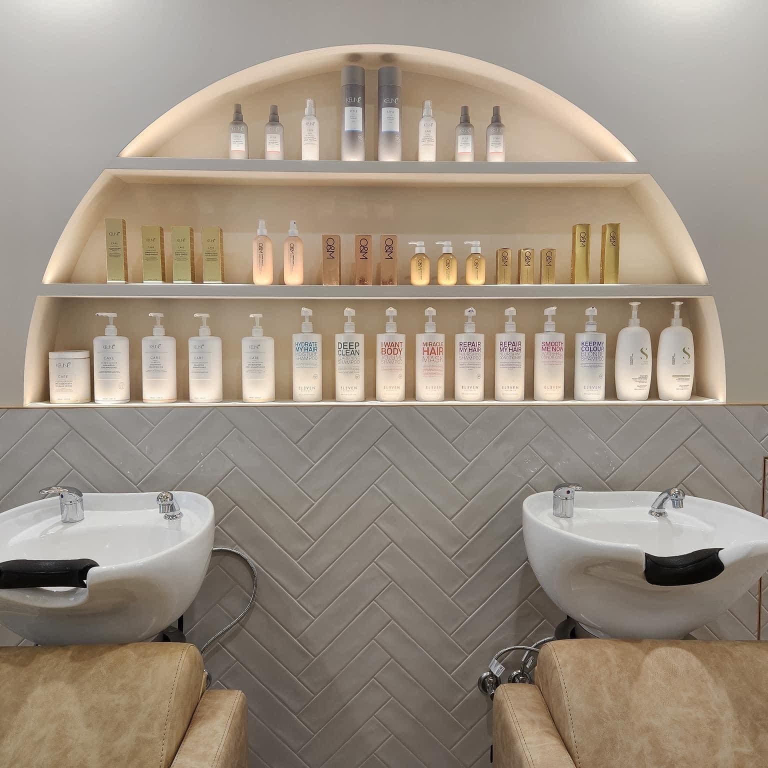 Commercial salon basin area with light grey ceramic herringbone splashback, matte finish, chrome taps and arched shelving.